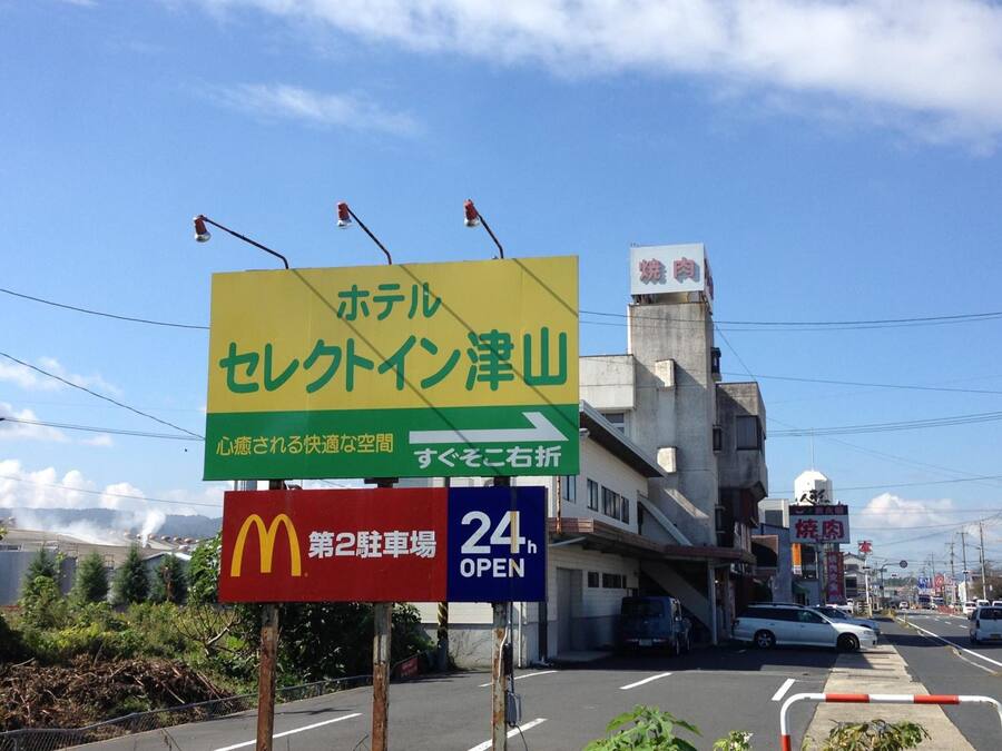 Une enseigne d’hôtel avec du texte en japonais, une enseigne de McDonald’s et une enseigne indiquant que l’établissement est ouvert 24 heures sur 24.