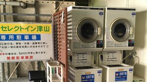 A laundry facility with stacked washing machines and dryers, a sign indicating a dedicated car parking area, and a caution sign about no parking. - Hotel Select Inn Tsuyama (Tsuyama)