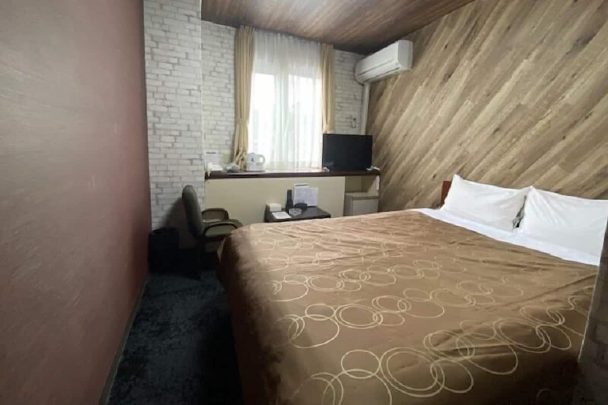 A hotel room with a bed, a desk with a chair, a television, and an air conditioning unit.