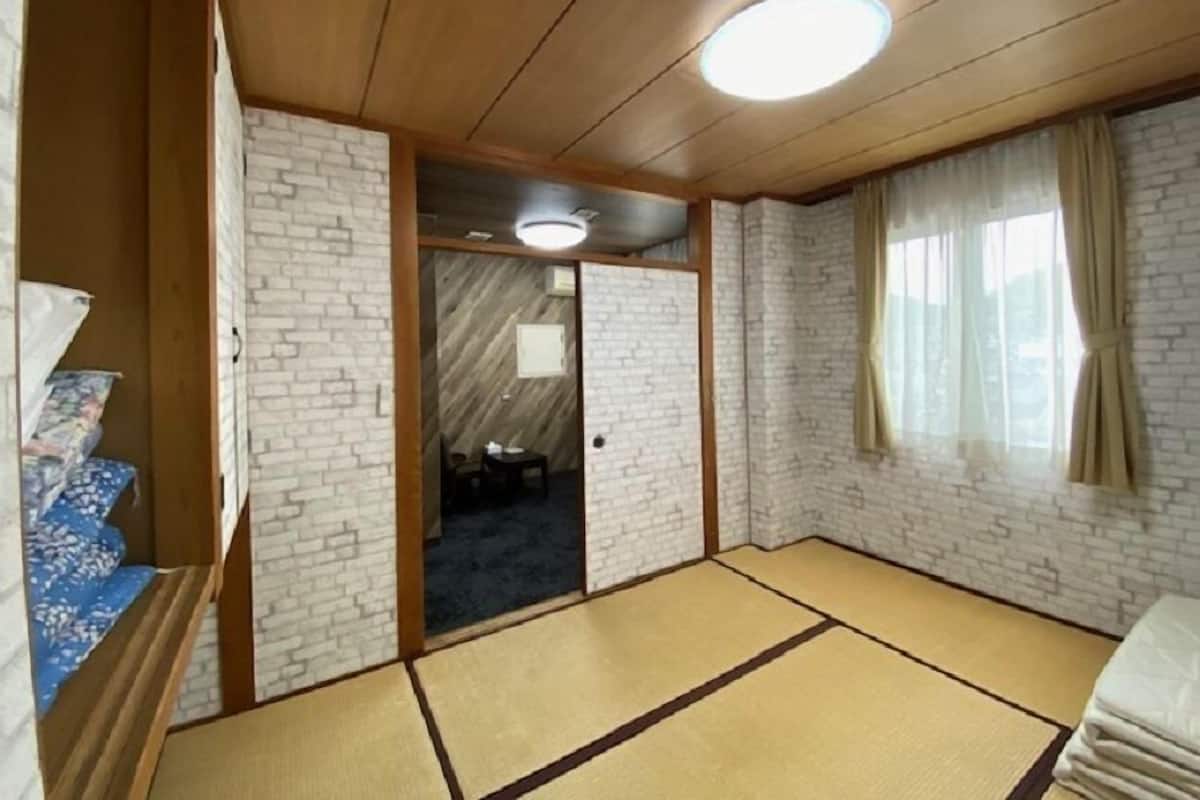 A room with tatami flooring, a wooden ceiling, and a brick wall.