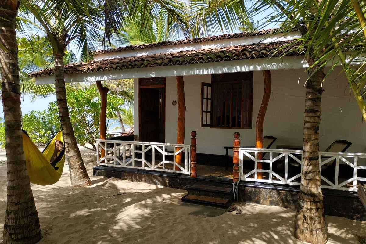 A beach house with a tiled roof, a porch with white railings, and a hammock.