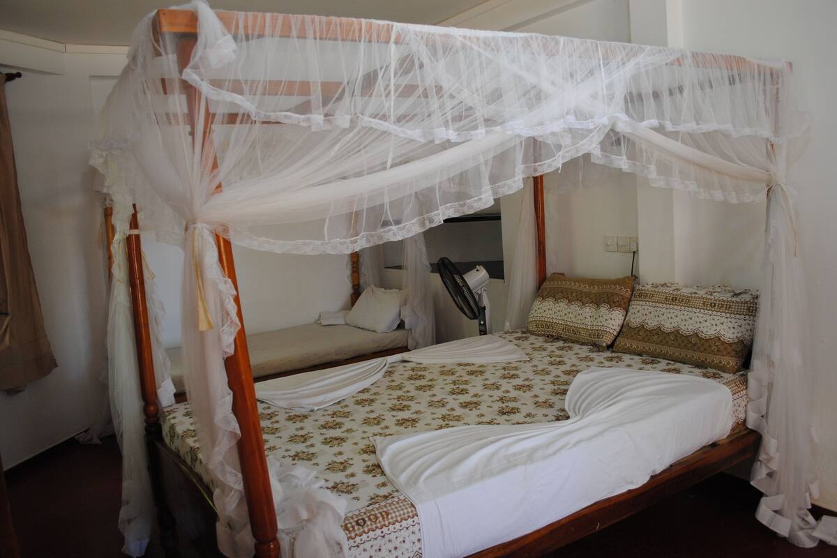 A four-poster bed with a canopy, a bedside table, and a chair.