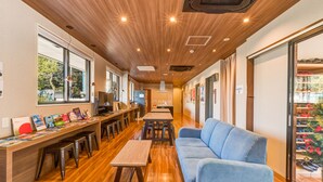 A modern interior with wooden flooring, a long bar area, and a seating area with a blue sofa. - Kintetsu Friendly Hostel Tennojipark Osaka (Osaka)
