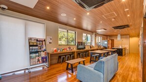A modern, well-lit room with wooden floors, a sofa, a TV, and a counter with various items. - Kintetsu Friendly Hostel Tennojipark Osaka (Osaka)