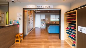 A reception area with a wooden bench, a shoe closet, and a blue couch. - Kintetsu Friendly Hostel Tennojipark Osaka (Osaka)