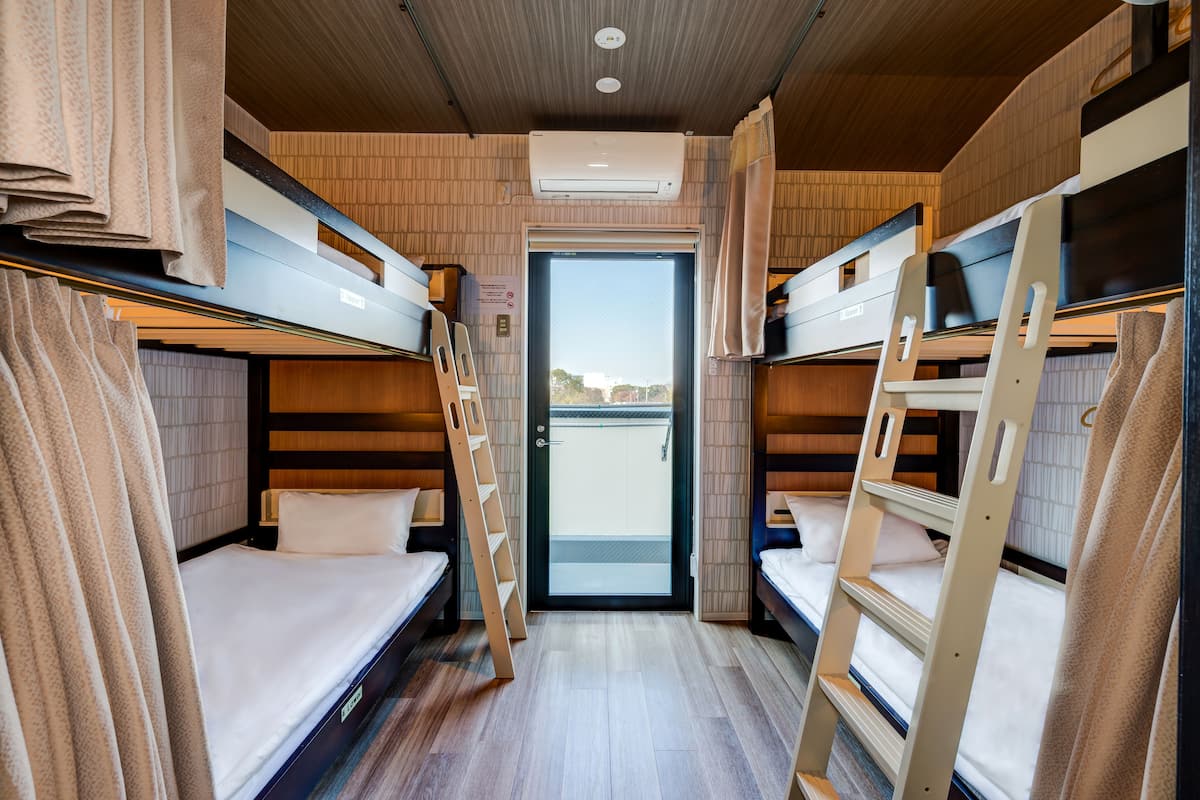 Habitación pequeña y luminosa con literas, una puerta que da al exterior y una escalera para acceder.