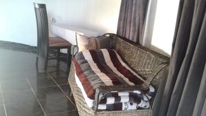 A wicker sofa with striped cushions, a small wooden chair, and a white bench against a wall.
