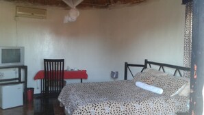 A bedroom with a bed, a chair, a table with a red tablecloth, a television, and a mosquito net above the bed.