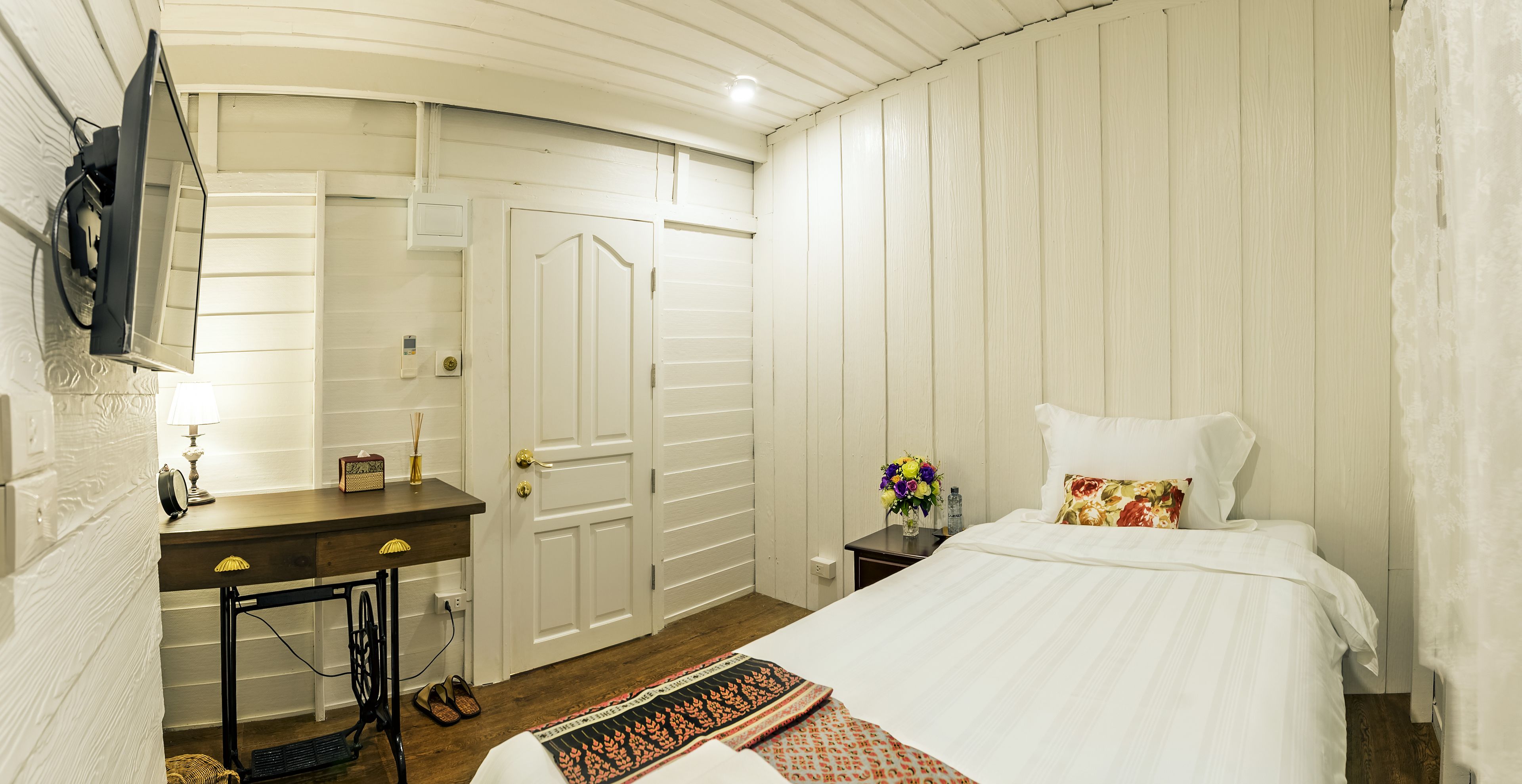 A bedroom with a bed, a desk, a chair, a lamp, and a door.