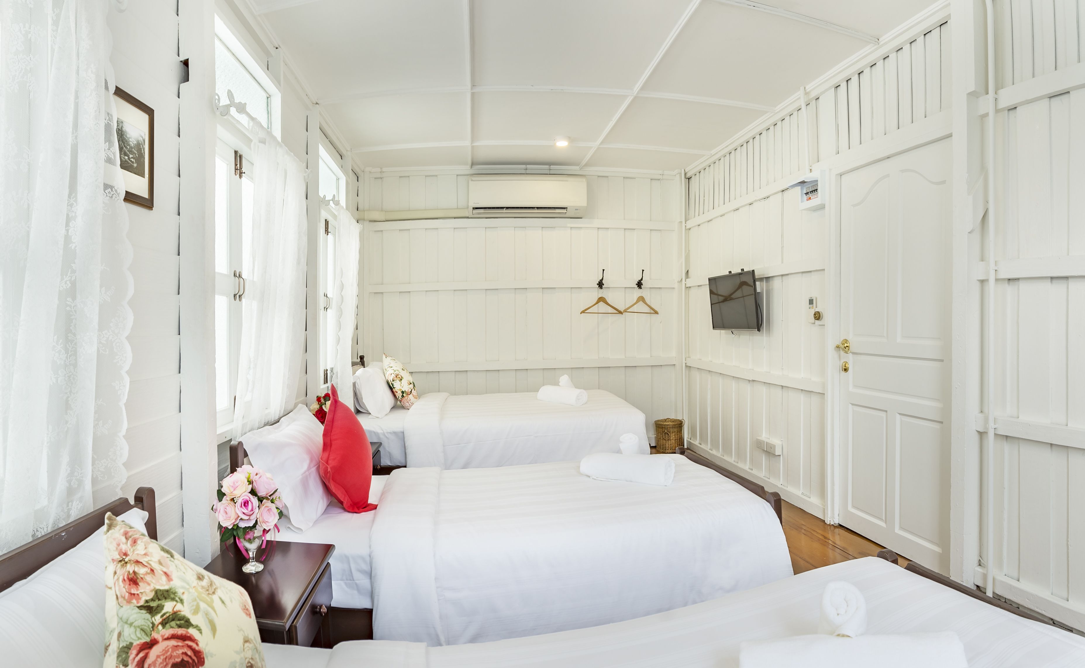 Habitación de hotel con dos camas, una ventana con cortinas traslúcidas, un aire acondicionado de pared y una puerta con picaporte.