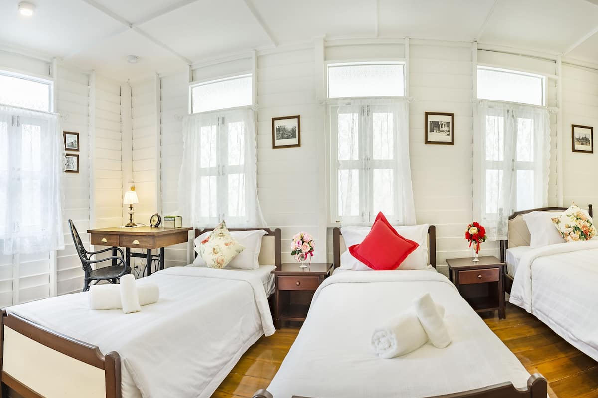 Hotellihuone, jossa on kolme erillistä sänkyä, työpöytä tuolilla sekä yöpöytä lampulla.