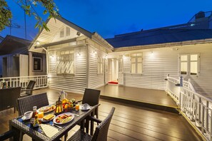 A well-lit outdoor dining area with wicker furniture and a table set for breakfast. - Baan Kachitpan (Bangkok)
