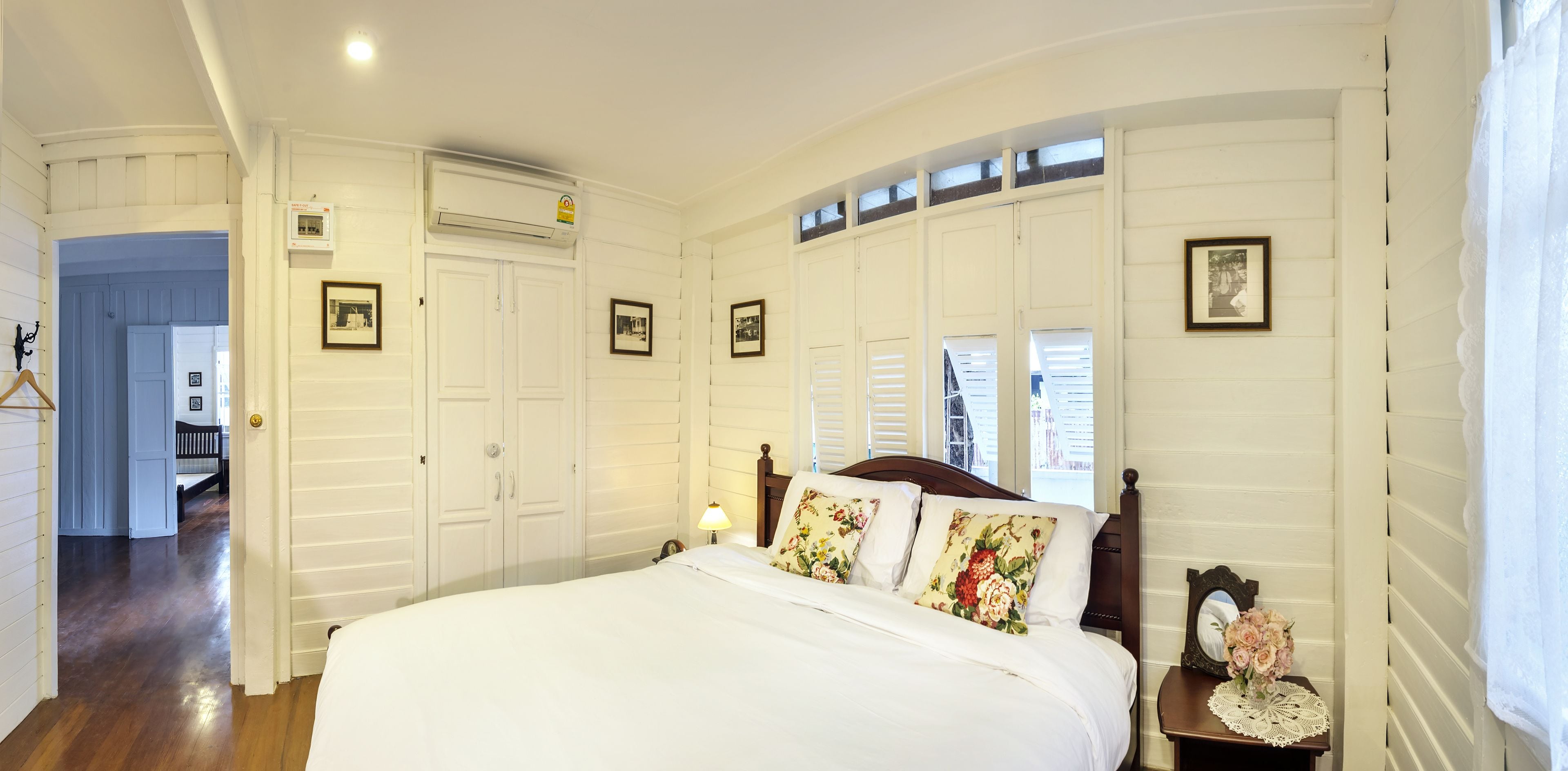 A bedroom with a large bed, white walls, wooden floor, and a wardrobe with a mirror and pictures.