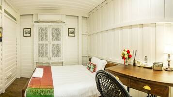 Una habitación de hotel con cama, un escritorio de madera, un espejo y una ventana con cortinas de encaje.