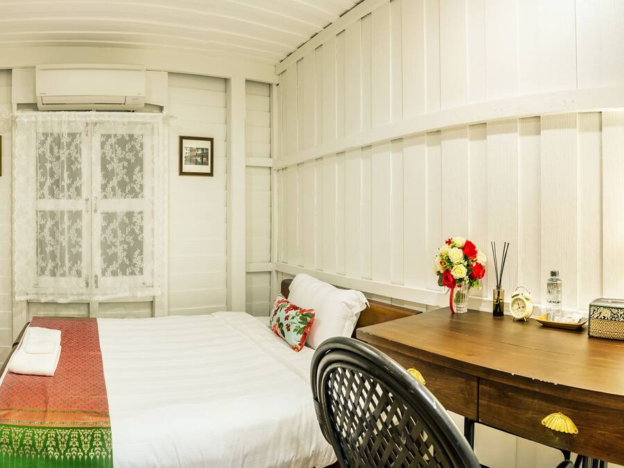 Una habitación de hotel con cama, un escritorio de madera, un espejo y una ventana con cortinas de encaje.