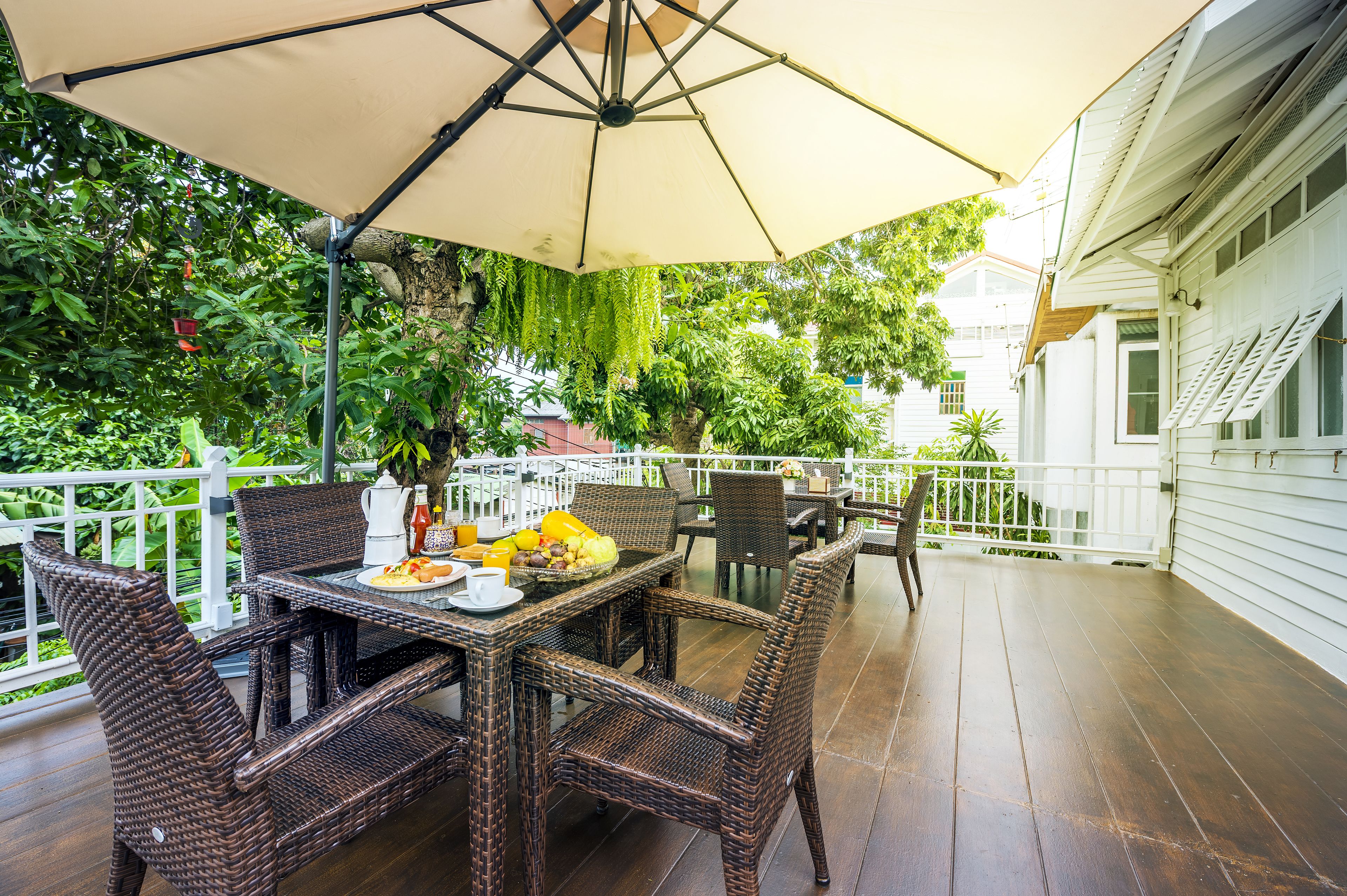 An outdoor patio with wicker furniture, a table set with plates, cups, and a fruit bowl.