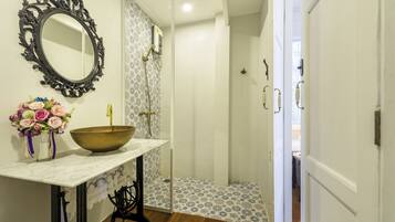 A bathroom with a large mirror, a sink with a bowl, and a shower area.