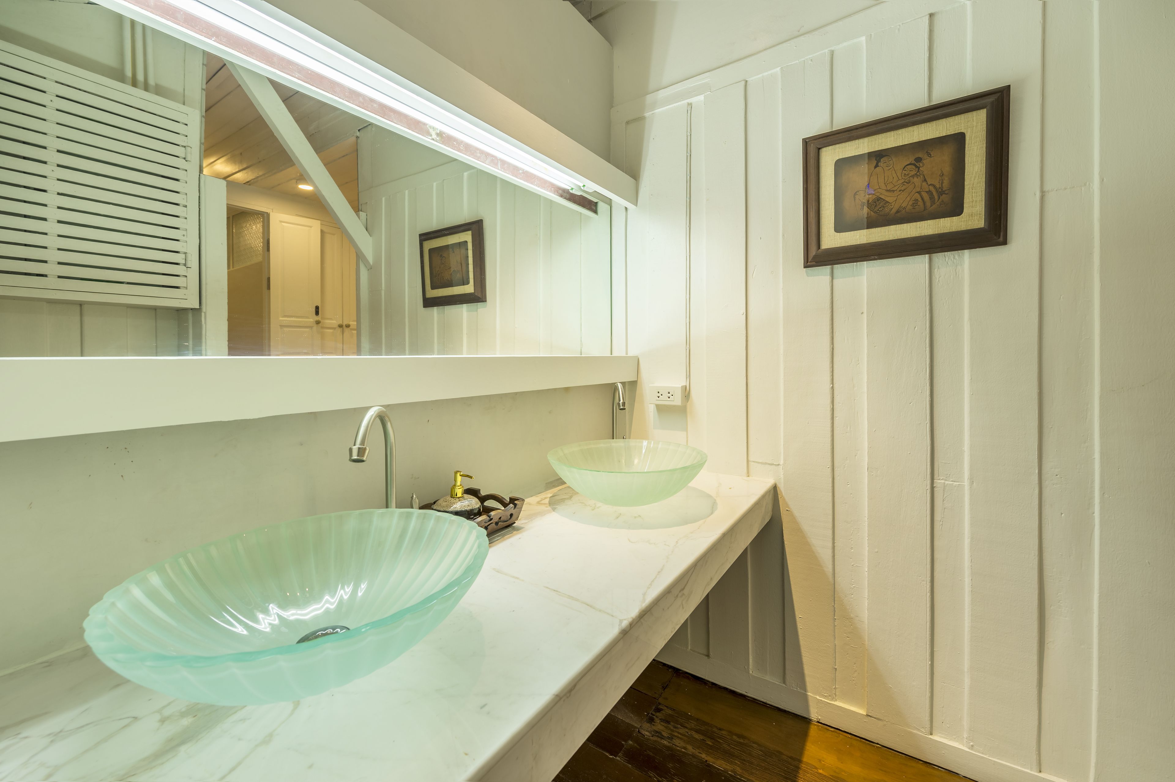 Une salle de bain avec un meuble-lavabo blanc, deux bols en verre, un miroir et un tableau encadré au mur.
