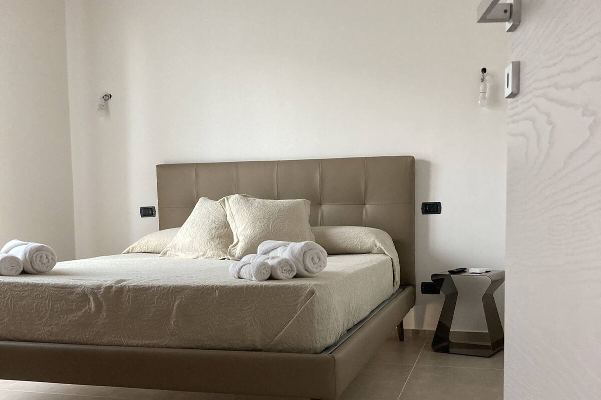 A modern bedroom with a large bed, a bedside table, and a wall-mounted light fixture.