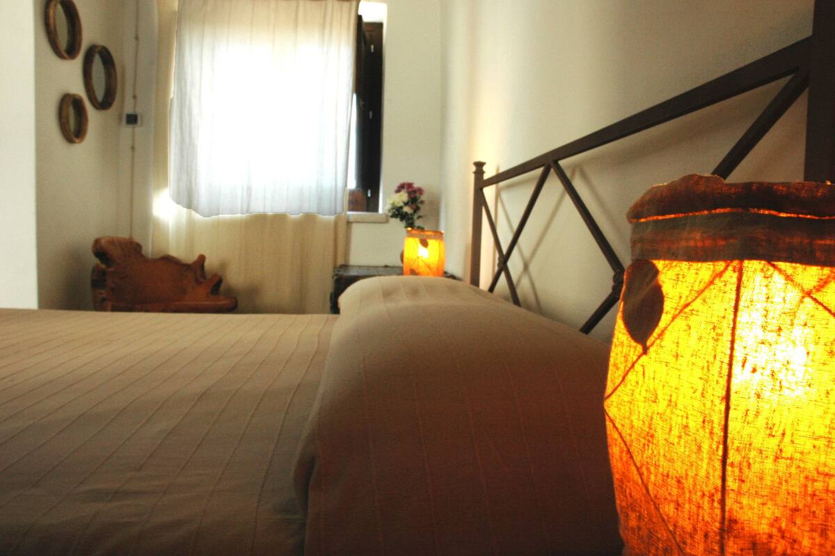 A bedroom with a bed, a nightstand with a lamp, and a window with curtains.