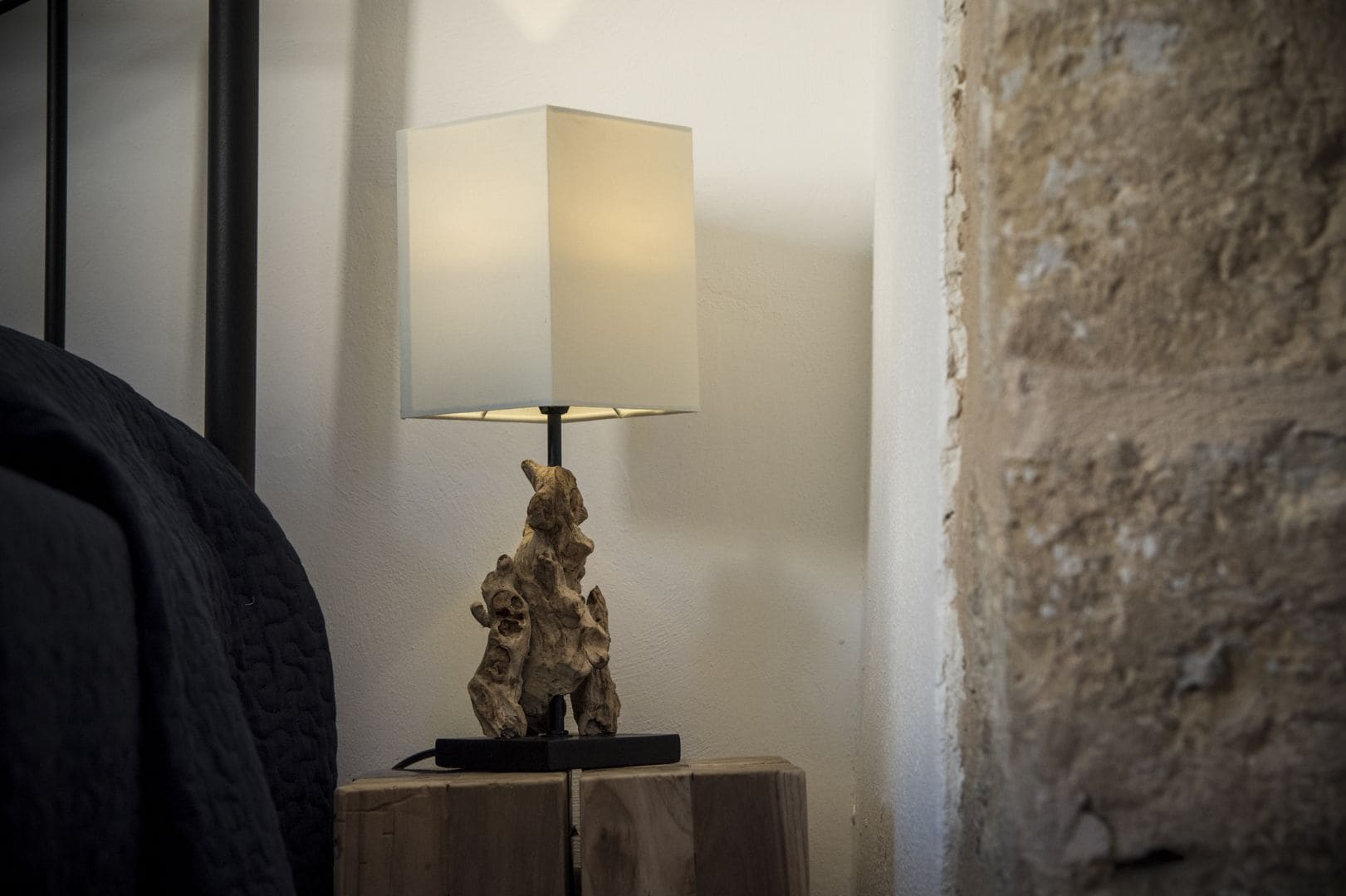 Una lámpara con pantalla cuadrada sobre una mesita de noche de madera.