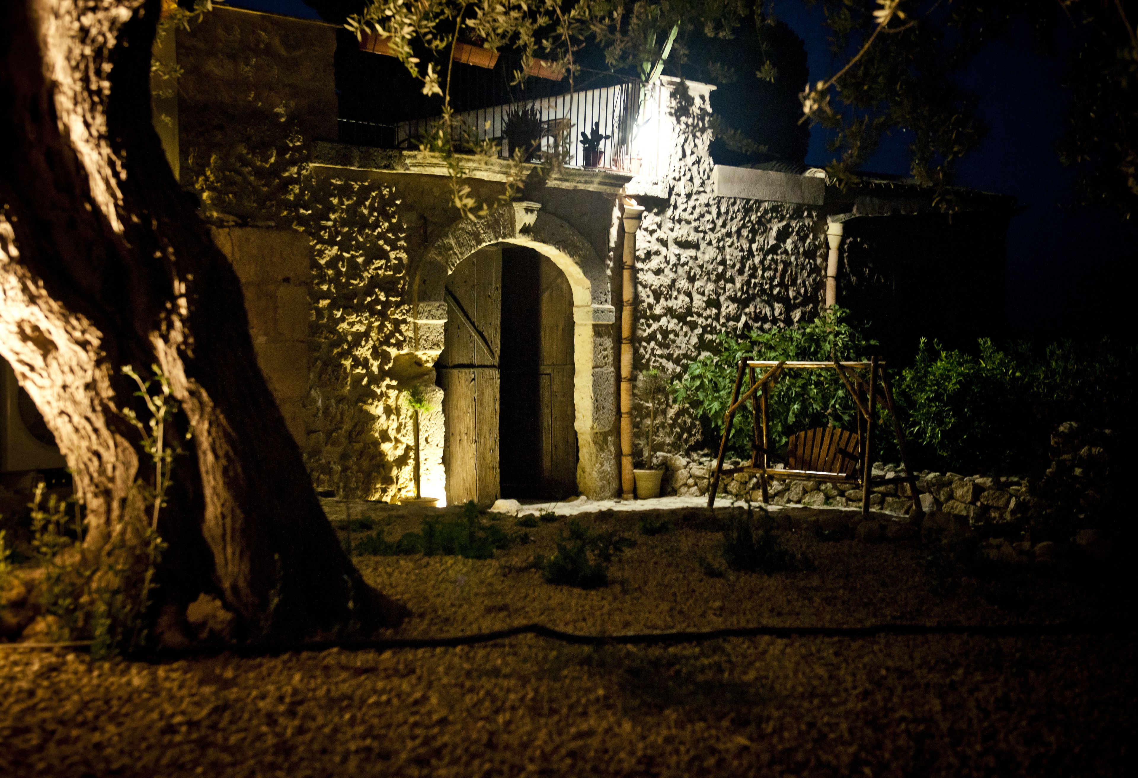 Un edificio de piedra con una entrada en arco, rodeado de vegetación y una silla de madera.