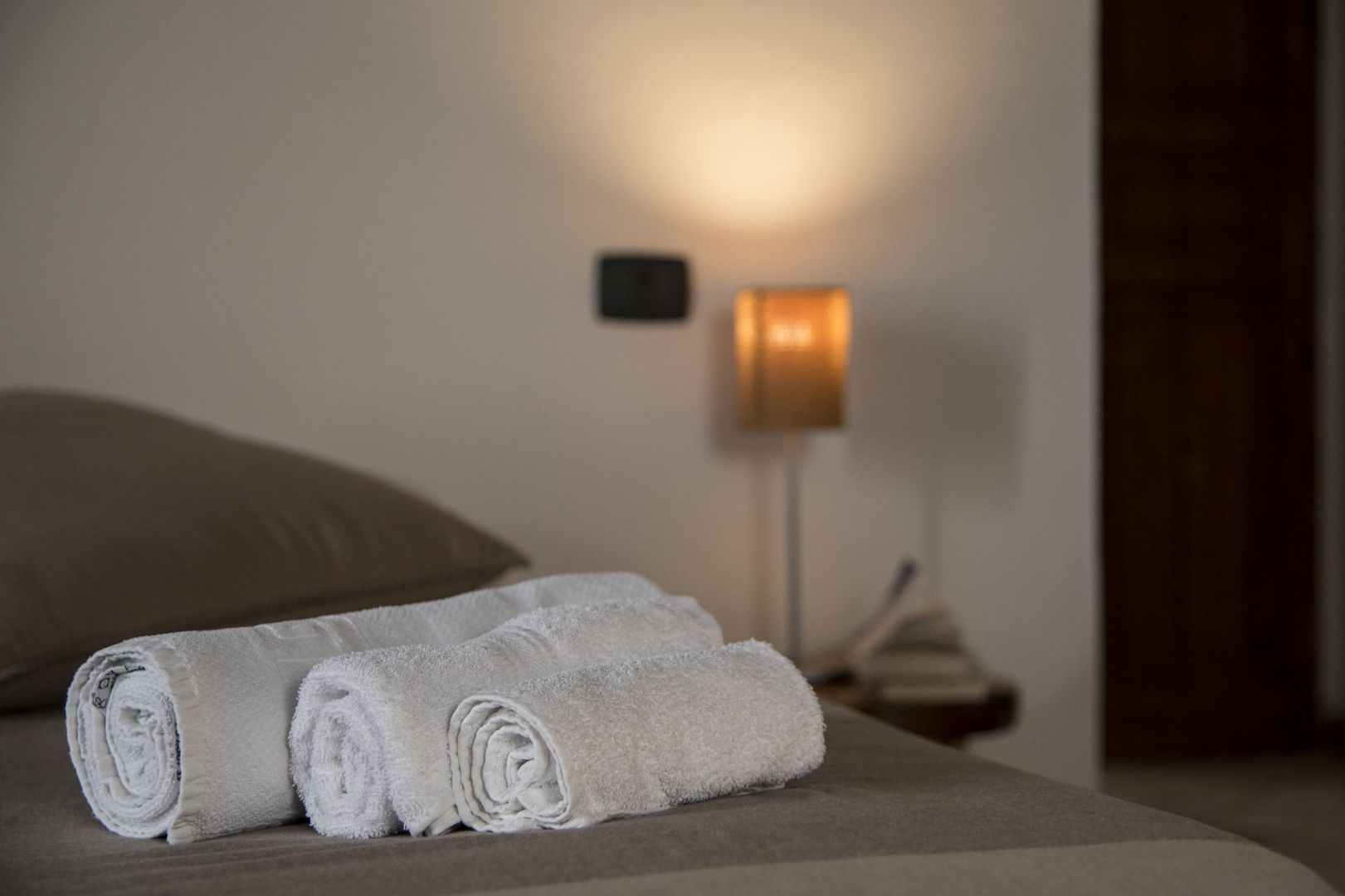 Un lit bien fait, avec des serviettes blanches pliées en rouleaux et une lampe de chevet.