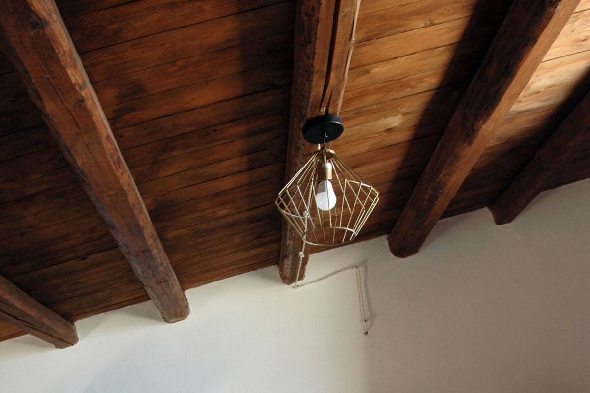 A bedroom with a wooden ceiling, a bed with floral bedding, two bedside tables with lamps, and a hanging light fixture.