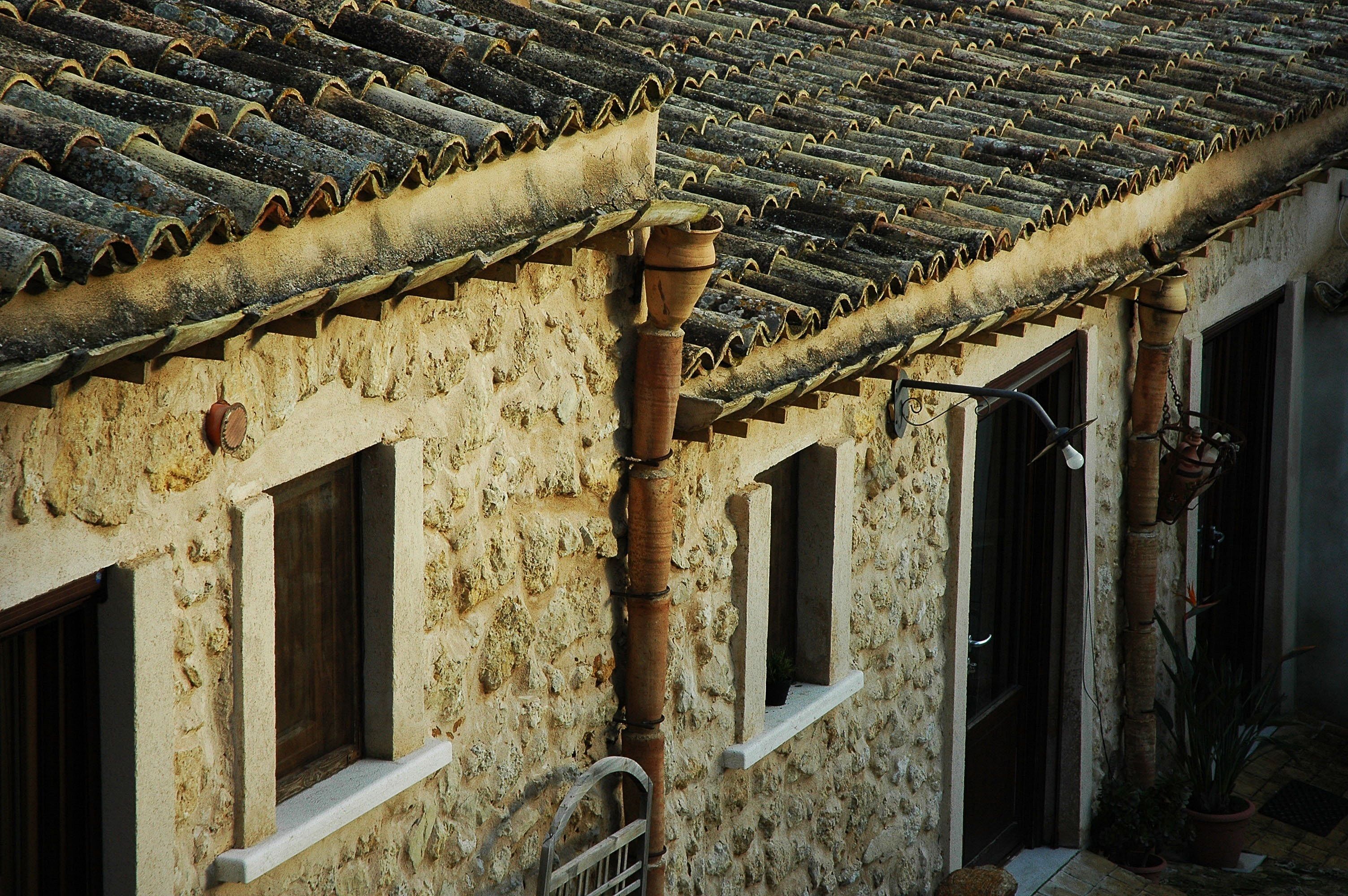 A building with a tiled roof and stone walls, featuring multiple windows and a small door.