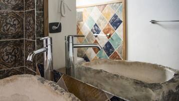Un baño con un lavamanos de piedra, dos grifos cromados y un salpicadero de mosaico colorido.