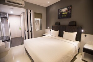 A modern hotel room with a large bed, a bedside table, a nightstand, a mirror, and a painting on the wall. - Happy Inn Melawai (Jakarta)