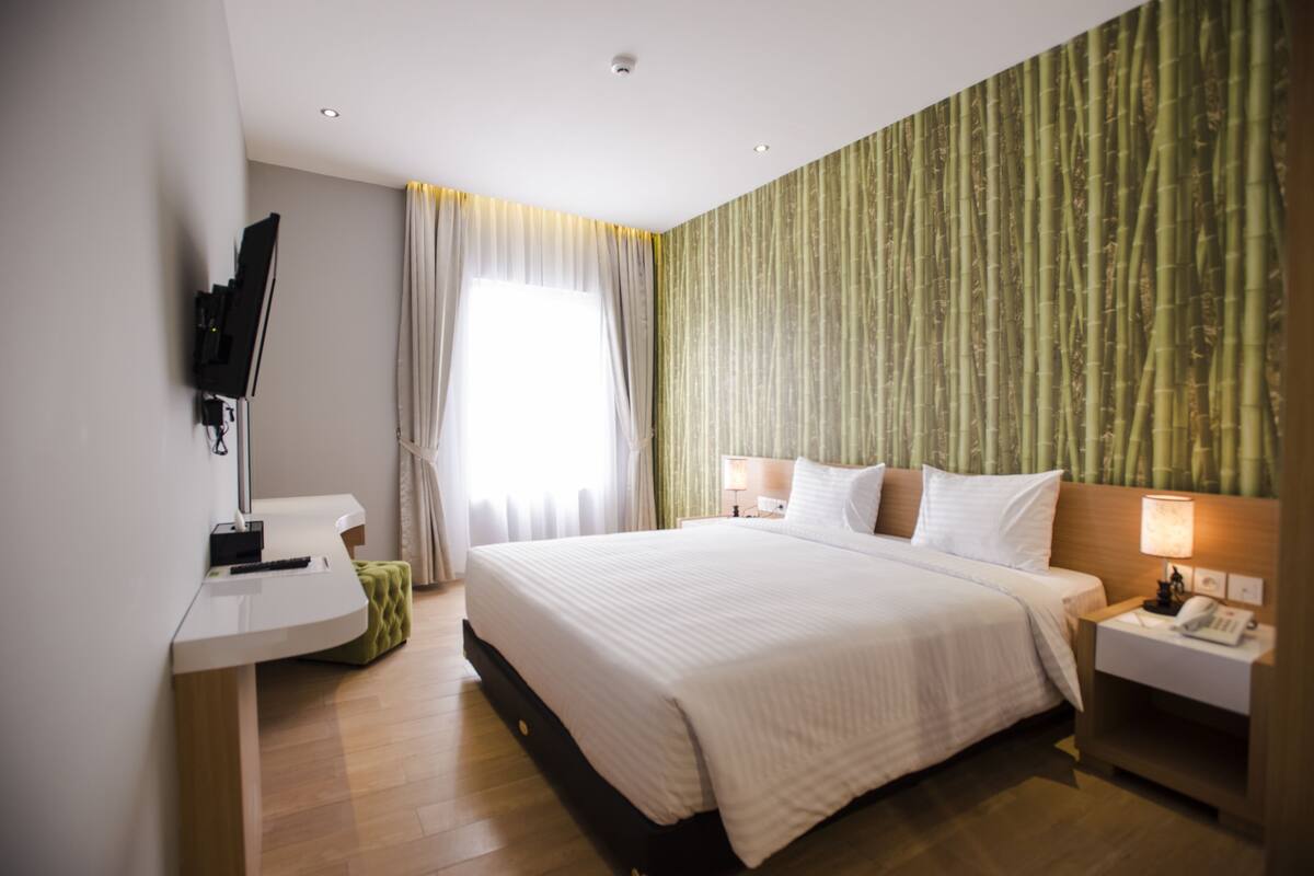 A modern hotel room with a large bed, bedside tables, a flat-screen TV, and a bamboo-patterned wall.