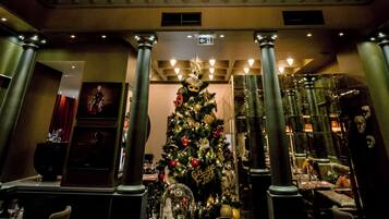 A chandelier with multiple arms and crystal details, a Christmas tree with decorations, and a glass ceiling with a view of the sky.