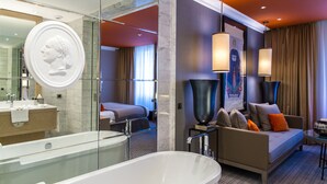 A modern hotel room with a large bathtub, a sofa, and a large mirror.