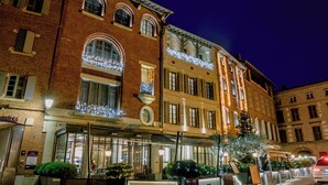 A multi-story hotel with a classic European architectural style, featuring arched windows and a balcony with string lights.
