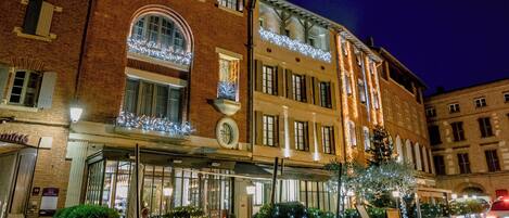 Un hotel de varios pisos con un estilo arquitectónico europeo clásico, con ventanas arqueadas y un balcón adornado con luces de cuerda.