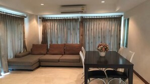 Una sala de estar con un sofá modular, una mesa de comedor con sillas y un jarrón con flores.
