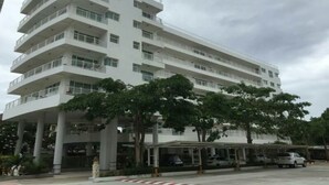 Un hotel de varios pisos con balcones, un estacionamiento techado y árboles en la fachada.