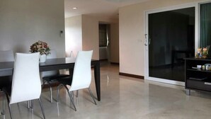 Un comedor moderno con una mesa oscura y sillas blancas, una planta en maceta y un ventanal corredizo que da a un balcón.