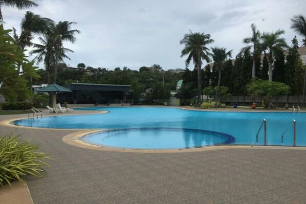 A large outdoor swimming pool surrounded by palm trees and lounge chairs.