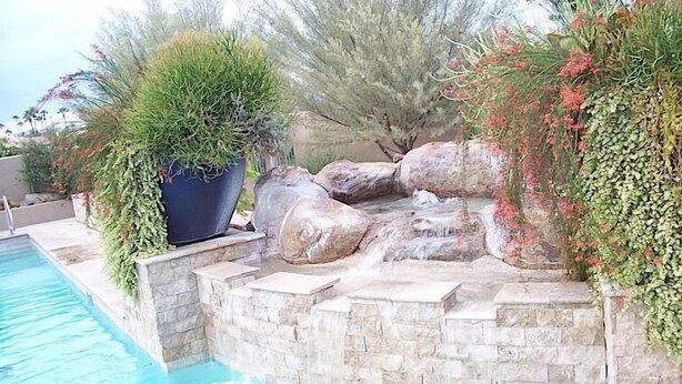 A pool area with a rock waterfall and surrounding greenery. - Rio Verde Townhouse By Signature Rentals (Rio Verde)