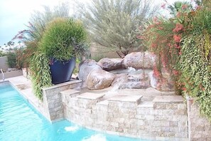 A pool area with a rock waterfall and surrounding greenery. - Rio Verde Townhouse By Signature Rentals (Rio Verde)