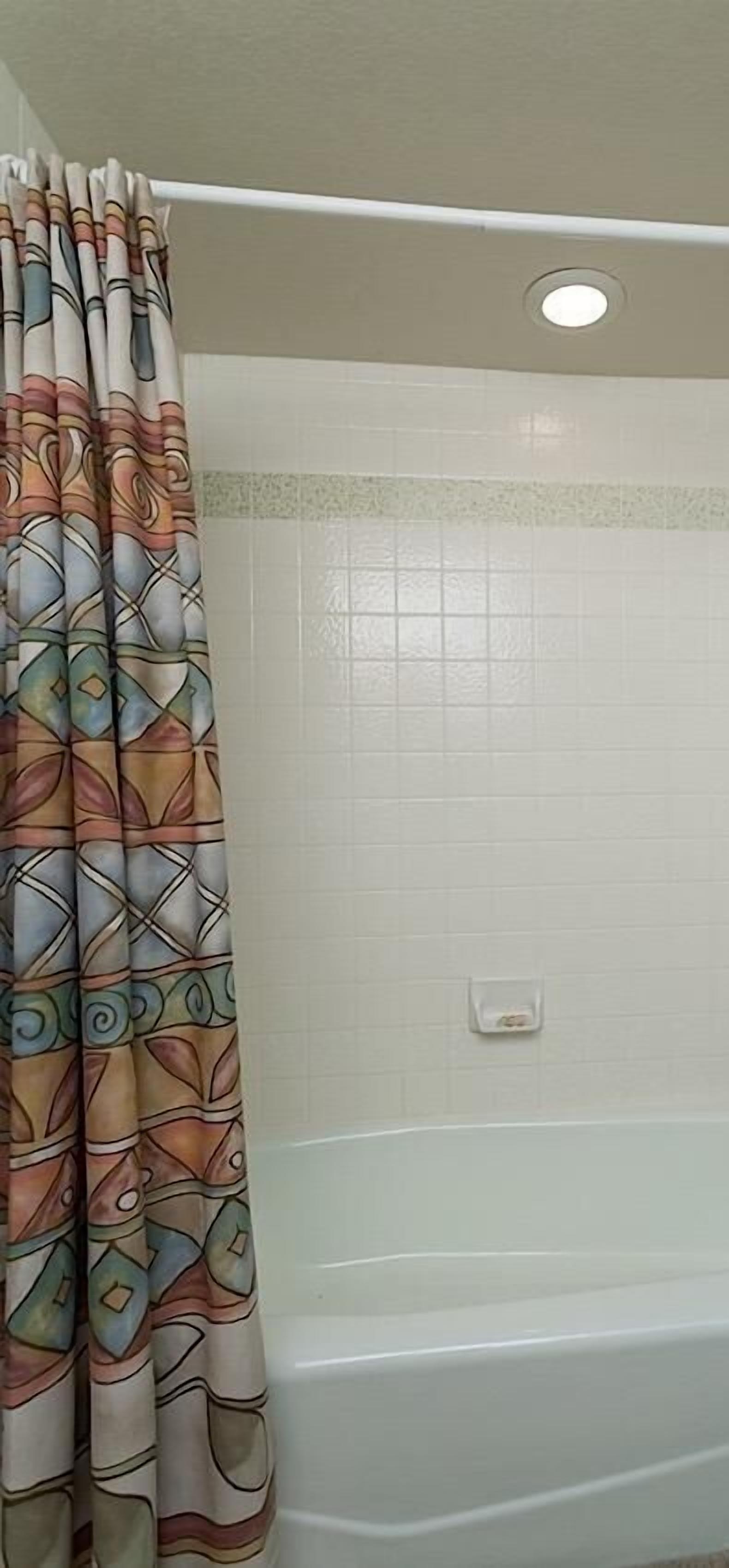 Ein Badezimmer mit Duschvorhang mit geometrischem Muster, einer weißen Badewanne und einer kleinen Seifenschale an der Wand.