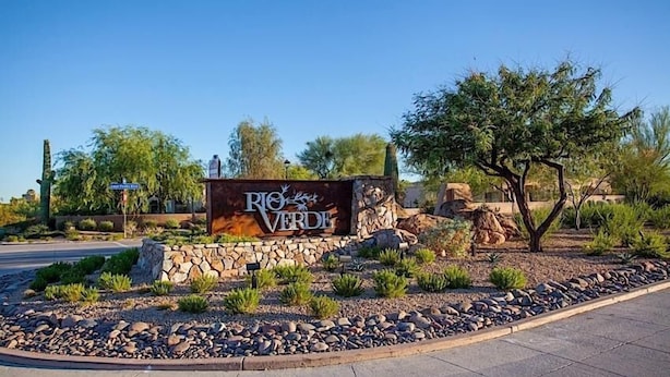 A sign for Rio Verde with a stone wall and desert landscaping.