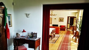 A living room with a wooden floor, a red carpet, a dining table with chairs, a sofa, and a chandelier. - B&B Luna Di Langa (Alba)