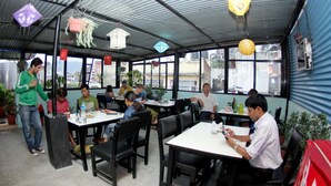A restaurant with tables and chairs, large windows, and hanging decorations. - Bag Packer's Lodge (Kathmandu)