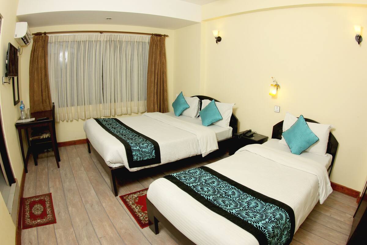 A hotel room with two beds, a desk, a chair, a red rug, and a window with curtains.