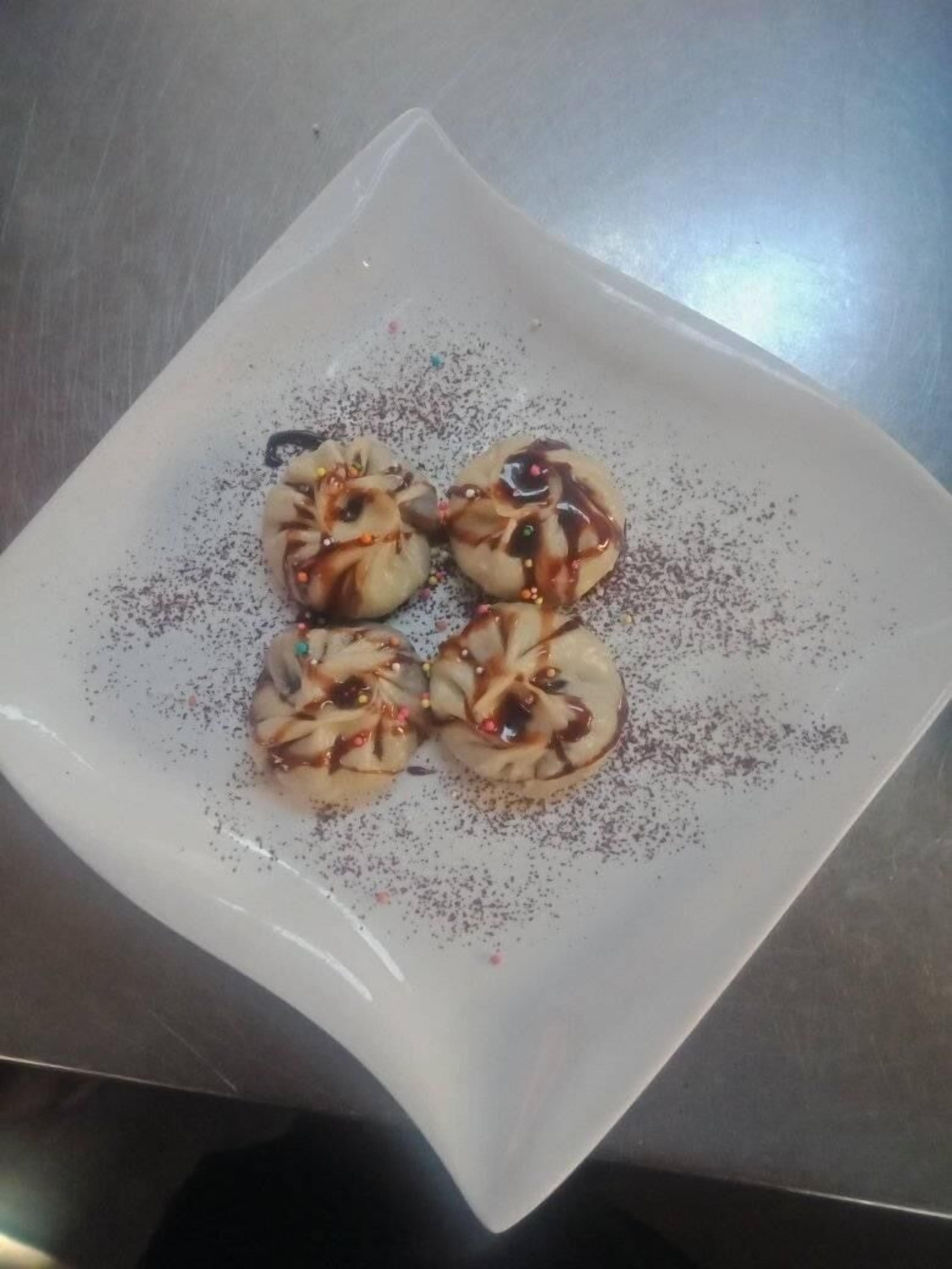 A white square plate with four dumplings topped with sauce and sprinkled with spices.