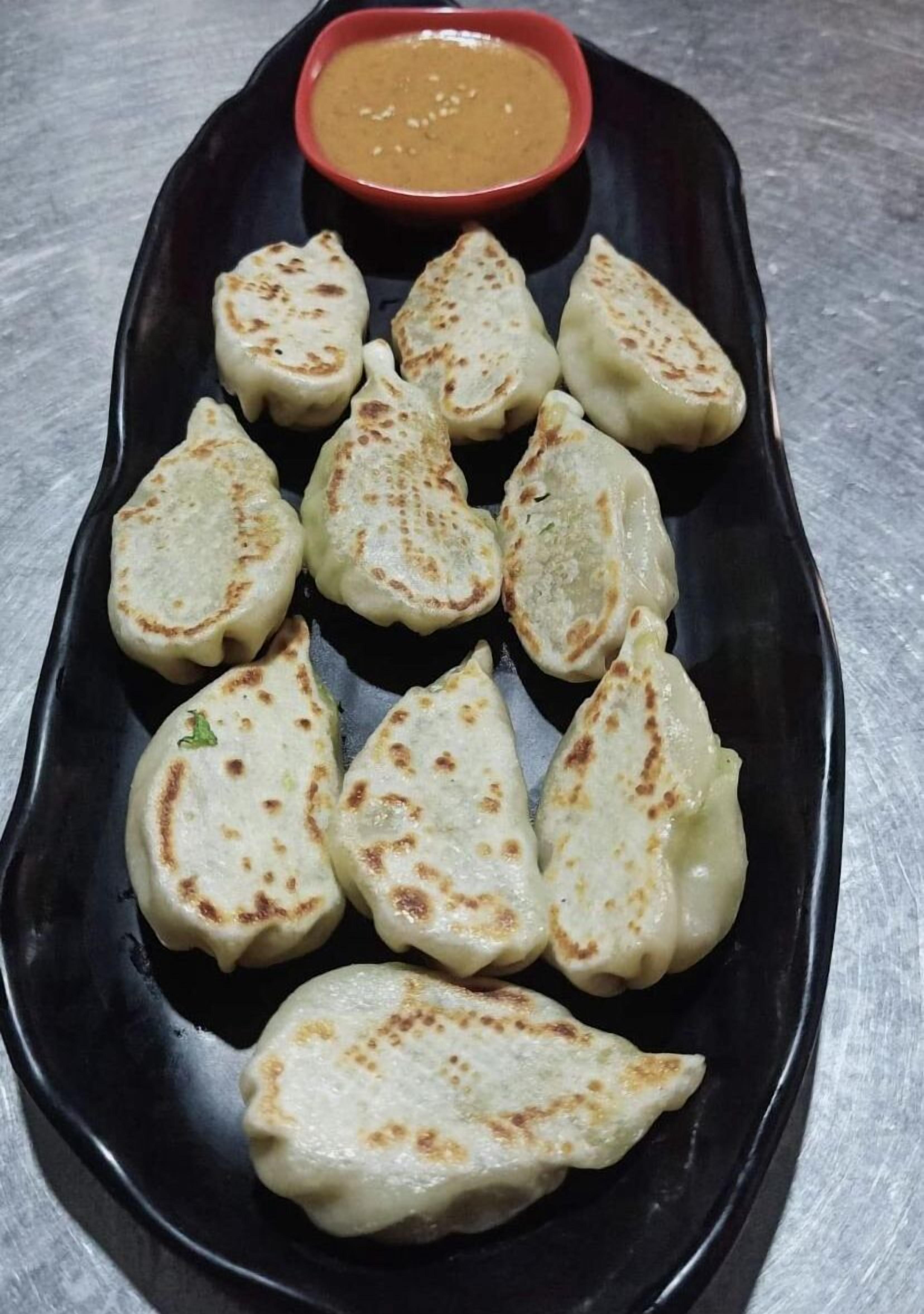 A black plate with several triangular-shaped dumplings and a small bowl of sauce.