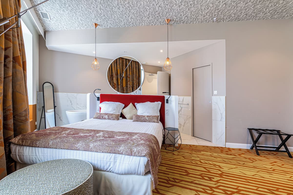 A hotel room with a large bed, a round mirror, a small table, and a patterned carpet.